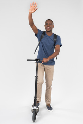 Smiling black male city tourist standing on scooter and waving