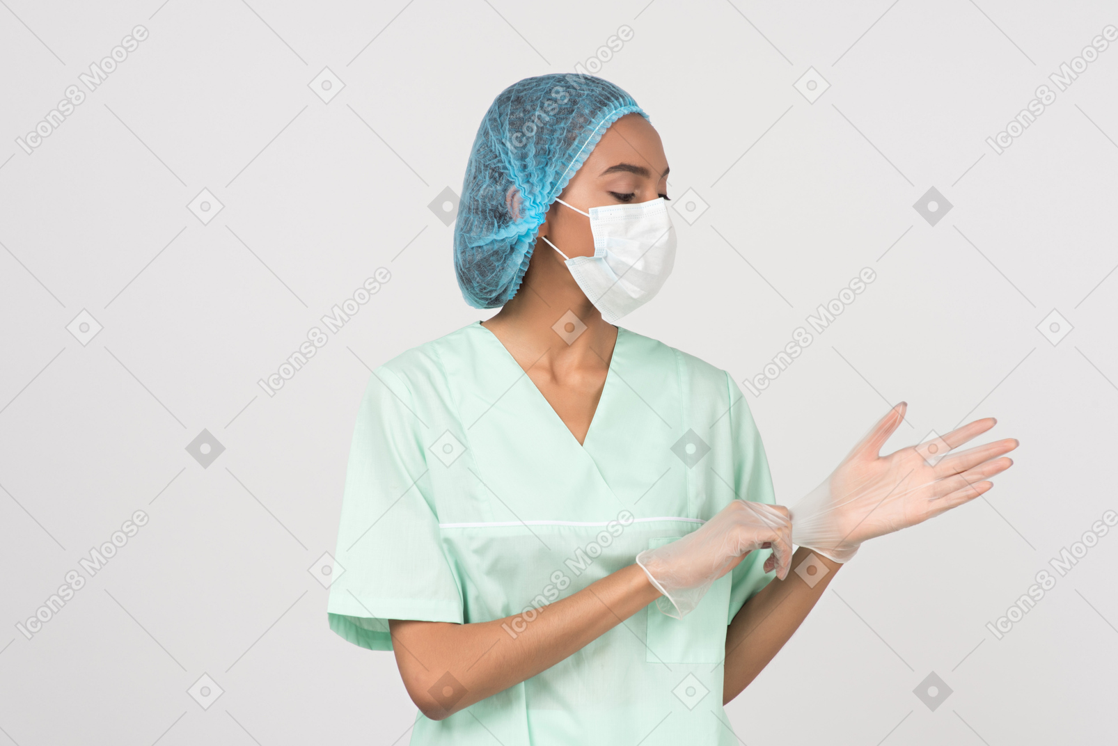 Une jeune femme dans un chapeau chirurgical et un masque facial mettant des gants