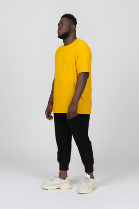 Three-quarter view of a thoughtful young dark-skinned man in yellow t-shirt
