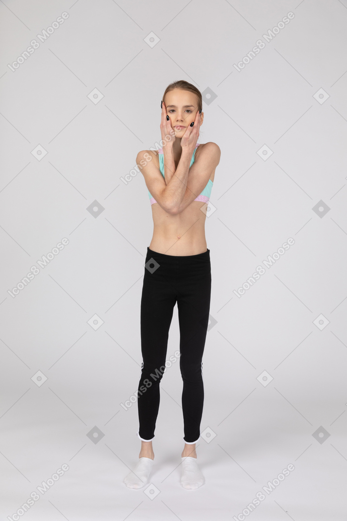 Vista frontal de una jovencita en ropa deportiva cruzando las manos y tocando las mejillas