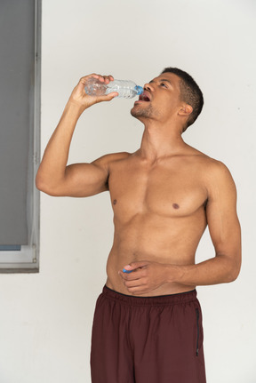 Bare chested young man in sport shorts drinking water