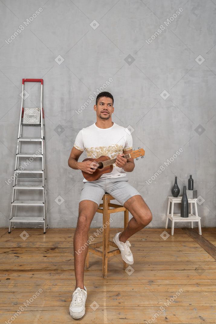 Vorderansicht eines mannes auf einem hocker, der ukulele spielt