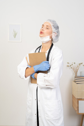 Three-quarter view of a sleepy young female doctor holding pencil and tablet