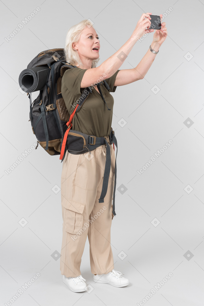 Mature female tourist carrying heavy backpack and making a photo
