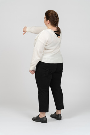 Женщина больших размеров в белом свитере показывает палец вниз