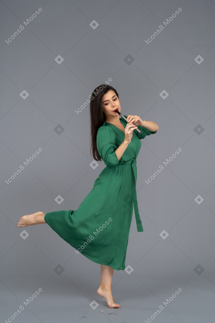 Vue latérale d'une jeune femme aux pieds nus en robe verte jouant de la flûte