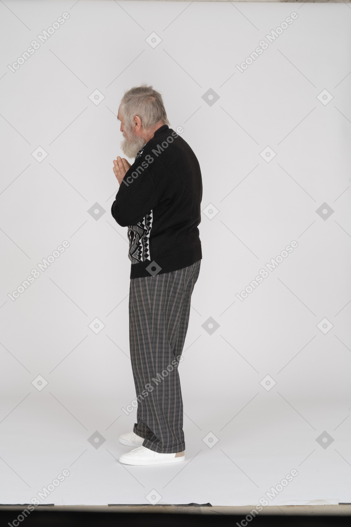 Vista laterale di un uomo anziano in piedi con le mani giunte