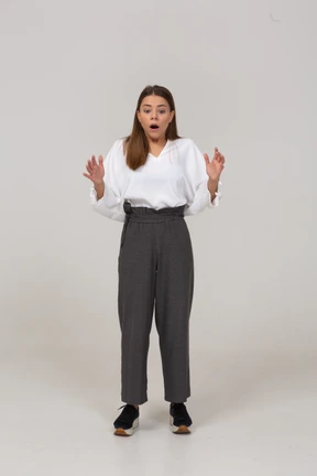 Front view of a shocked young lady in office clothing raising hands