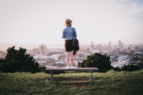 Junge frau, die auf einer bank steht und blick auf die stadt genießt