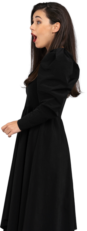 Vista laterale di una giovane donna sorpresa in un abito nero aprendo la bocca