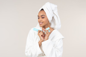 Black woman in white bathrobe and head towel enjoying her skin care routine