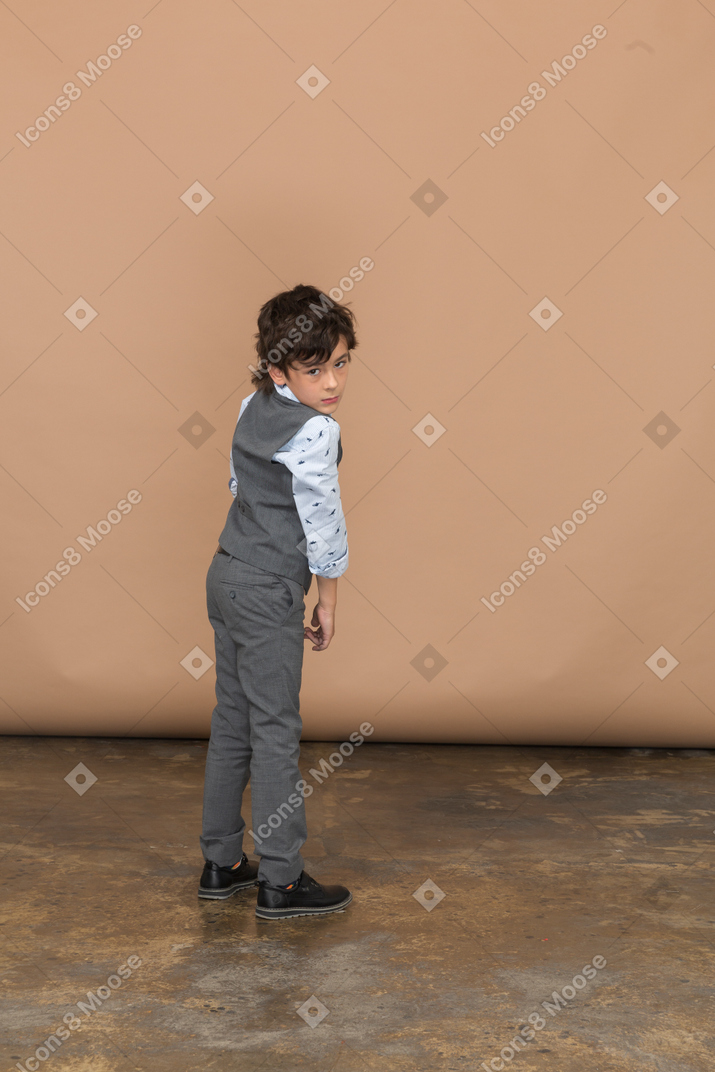 Vista traseira de um menino de terno cinza, olhando para a câmera