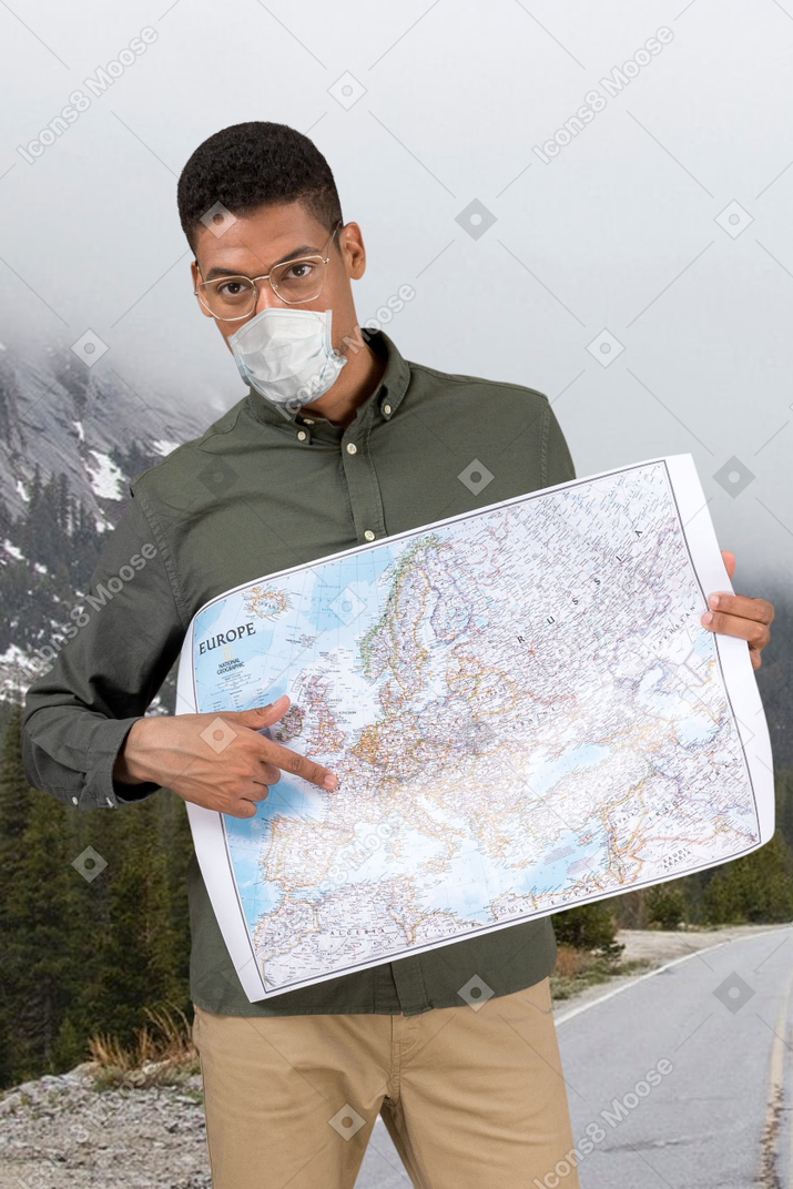 Homem de óculos e máscara facial apontando para um destino no mapa
