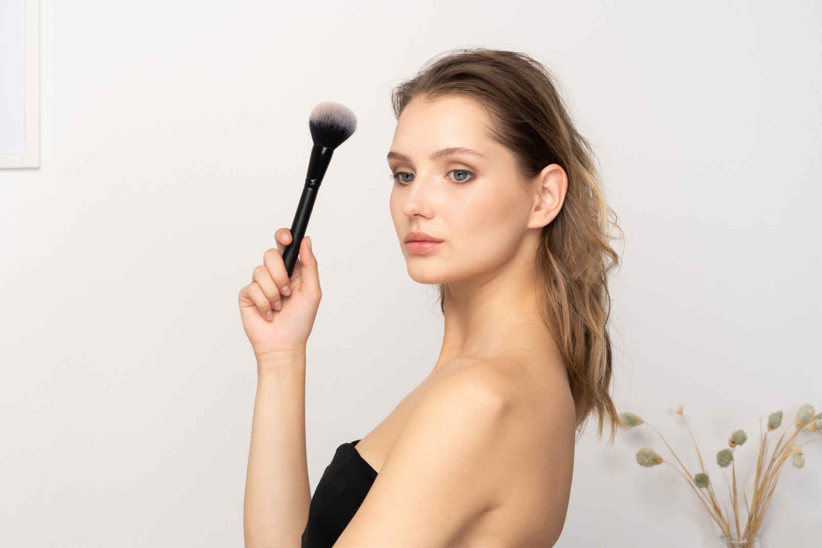 Side view of a sensual young woman holding a make-up brush & looking at camera
