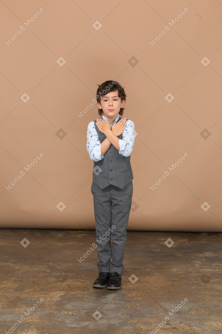 一个穿着西装的可爱男孩双手放在肩上站立的正面图