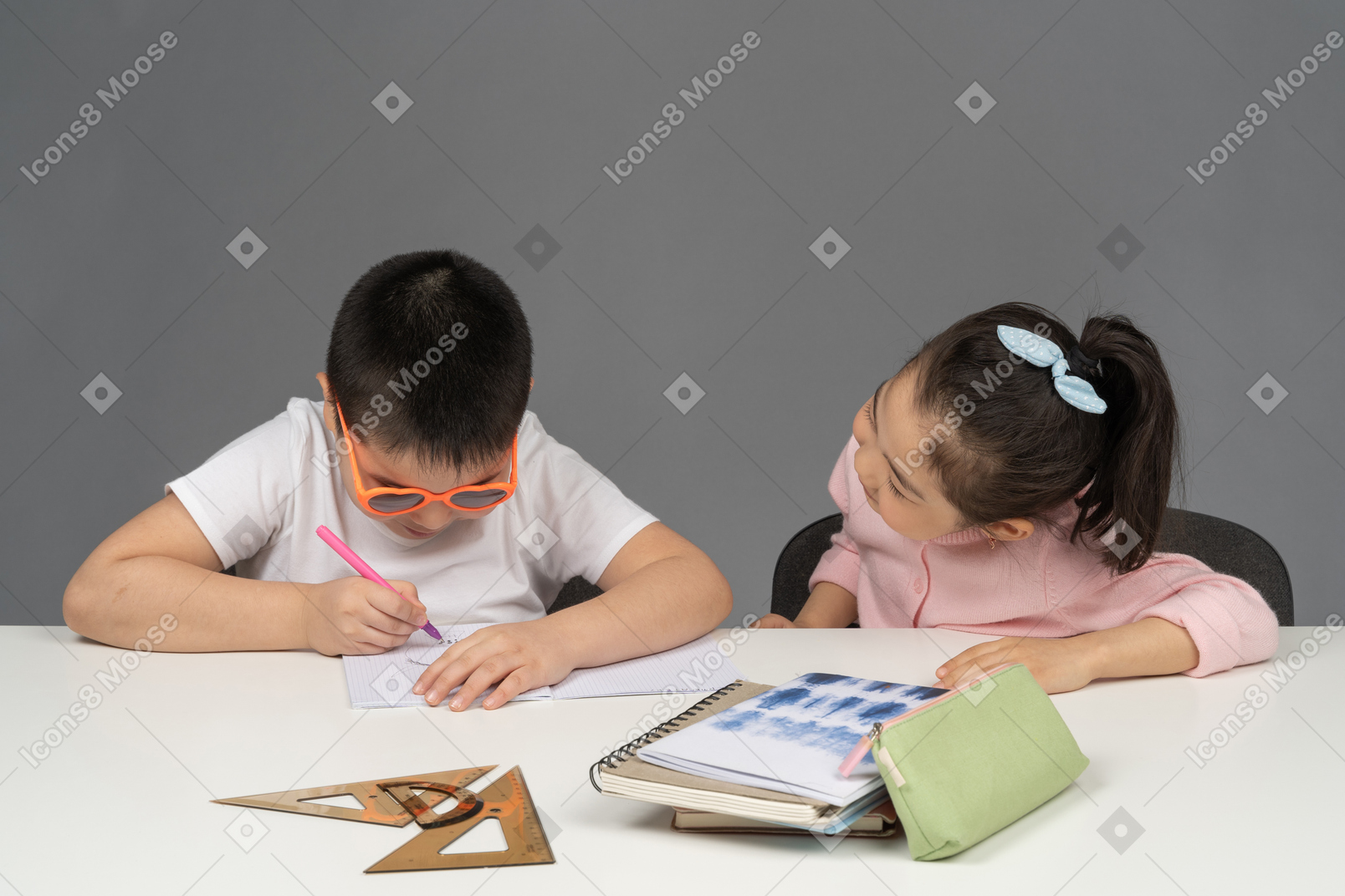 Boy in sunglasses doing homework next to his sister