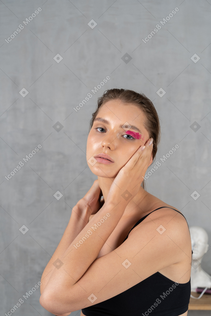 Side view of a young woman with bright pink eye make-up holding palm to cheek