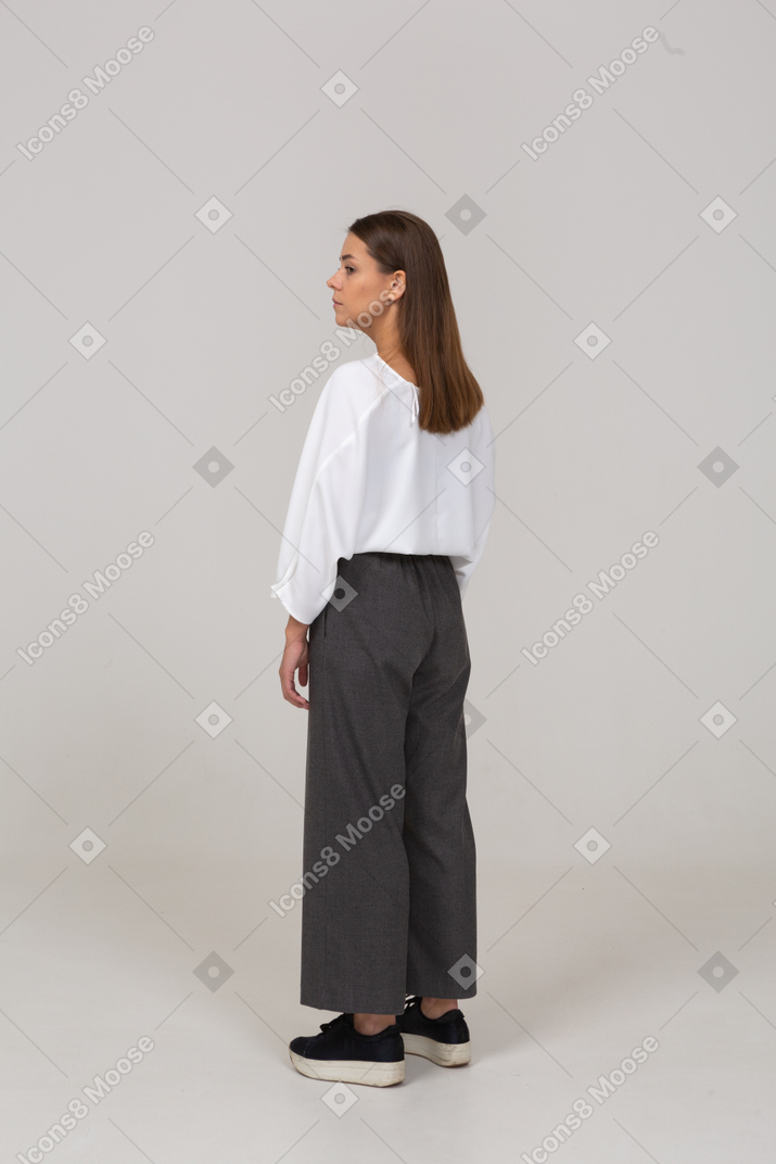 Vista posterior de tres cuartos de una joven en ropa de oficina mirando a un lado