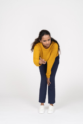 Front view of a girl in casual clothes bending down and making warning sign
