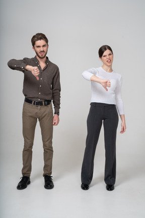 Vista frontale di una giovane coppia in abiti da ufficio che mostra il pollice verso il basso