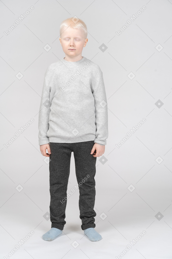 Full-length of a kid blonde boy standing still with his closed