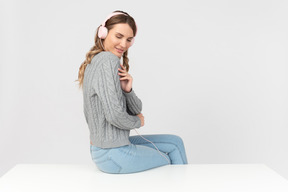 Mujer joven sentada en la mesa y disfrutando de la música en los auriculares