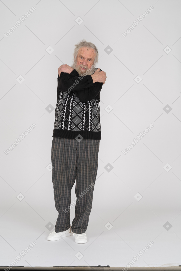 Пожилой мужчина стоит и обнимает себя