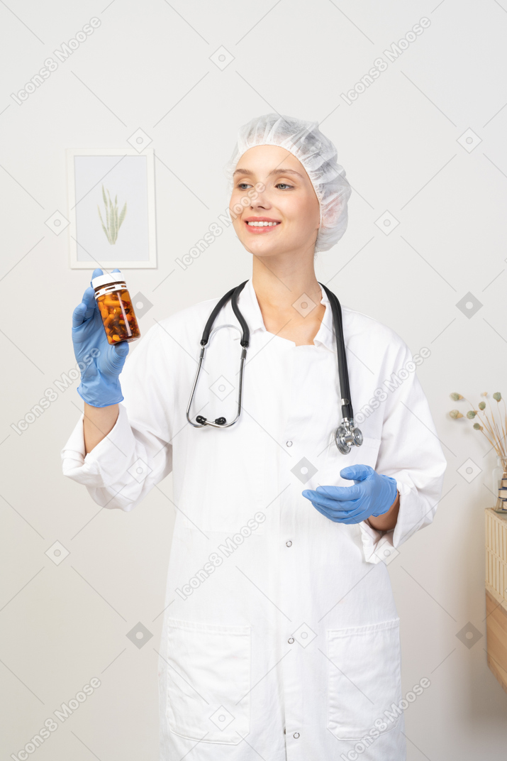 Vista frontale di una giovane dottoressa sorridente che tiene in mano un barattolo di pillole
