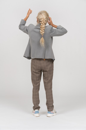 Back view of an old lady in suit standing with hand up