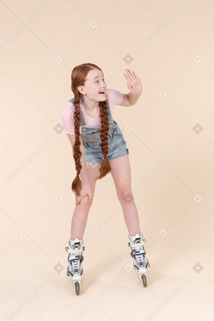 롤러 스케이트에 서서 손을 흔들며 십 대 아이 소녀