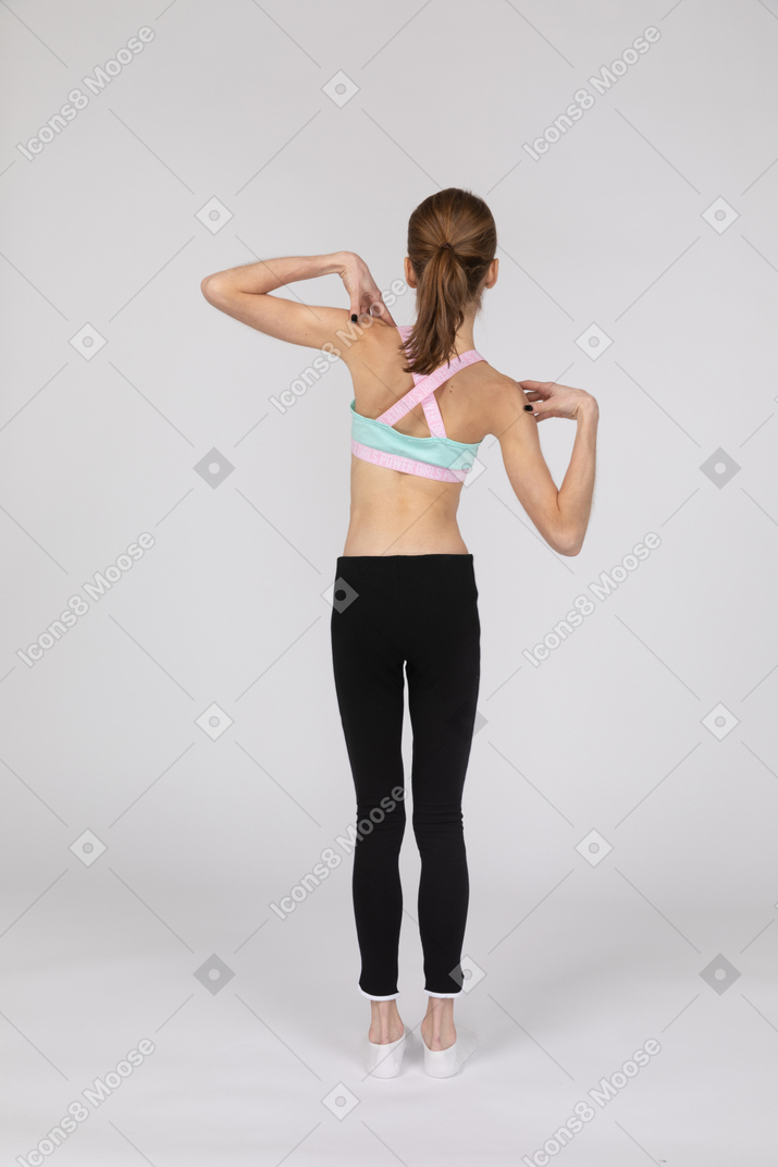 Back view of a teen girl in sportswear touching her shoulders and tilting right