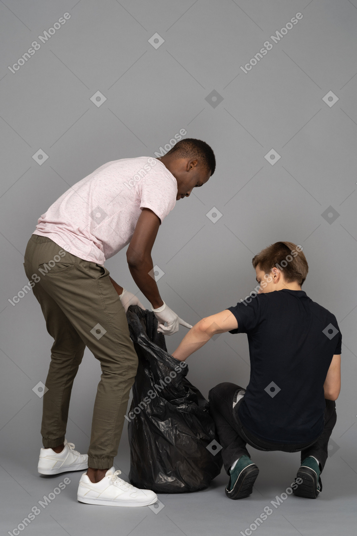 Two young men arranging a trash bag
