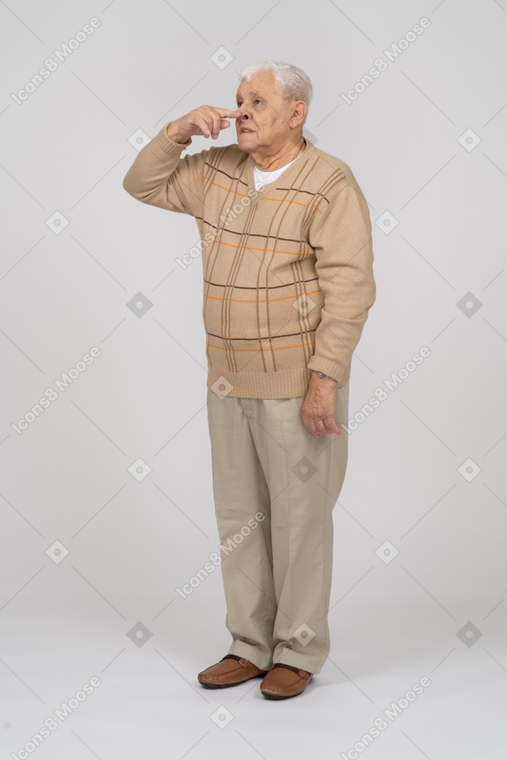 Front view of an old man in casual clothes touching nose