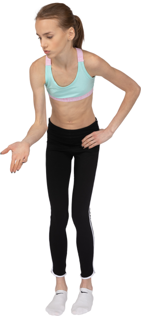 Vista frontal de uma adolescente em roupas esportivas apontando as mãos em algum lugar para baixo