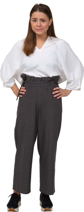 Front view of a confused young lady in office clothing putting hands on hips