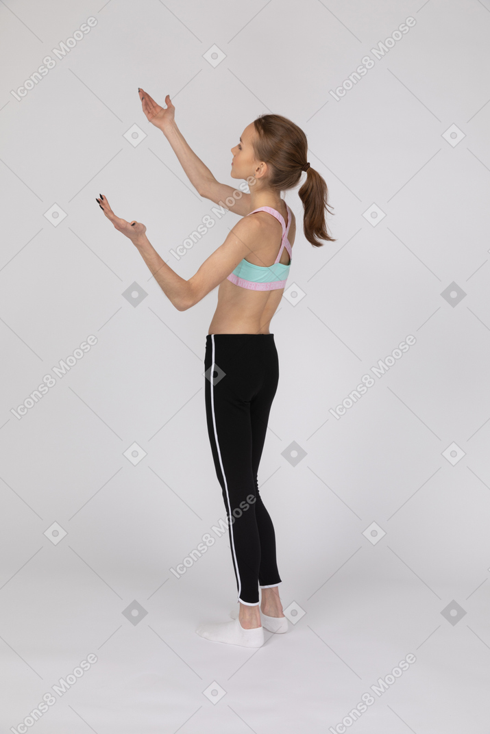 Vista lateral de una adolescente en ropa deportiva levantando las manos