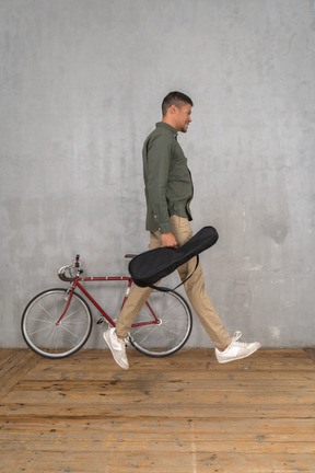 Side view of a man with a ukulele case jumping up