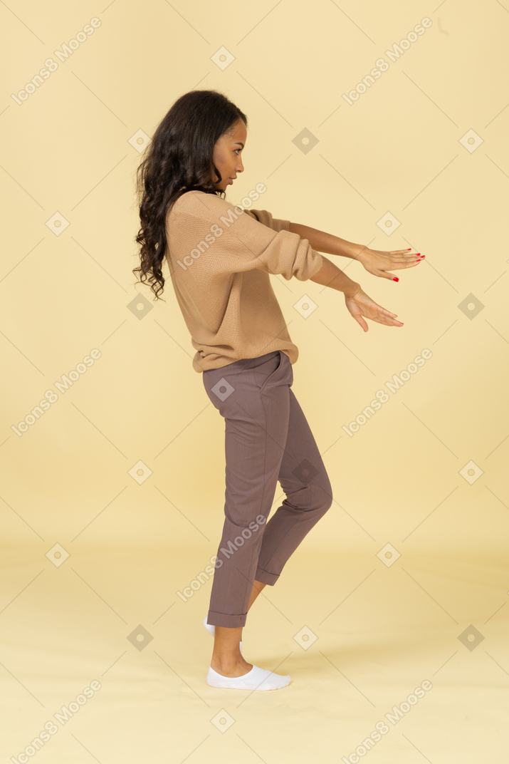 Side view of an unwilling dark-skinned young female outstretching hands