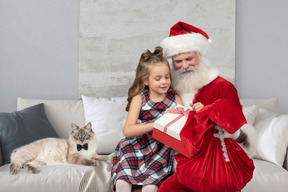 Kleines mädchen auf den knien des weihnachtsmanns bekommt ihre geschenke
