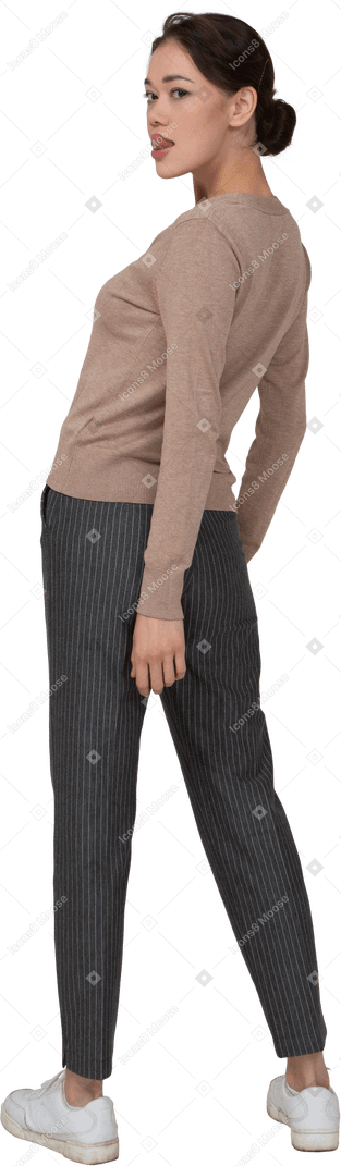 一位年轻的女士，穿着套头衫和裤子的四分之三后视图，显示舌头