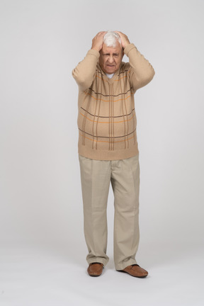 Front view of an old man in casual clothes suffering from headache