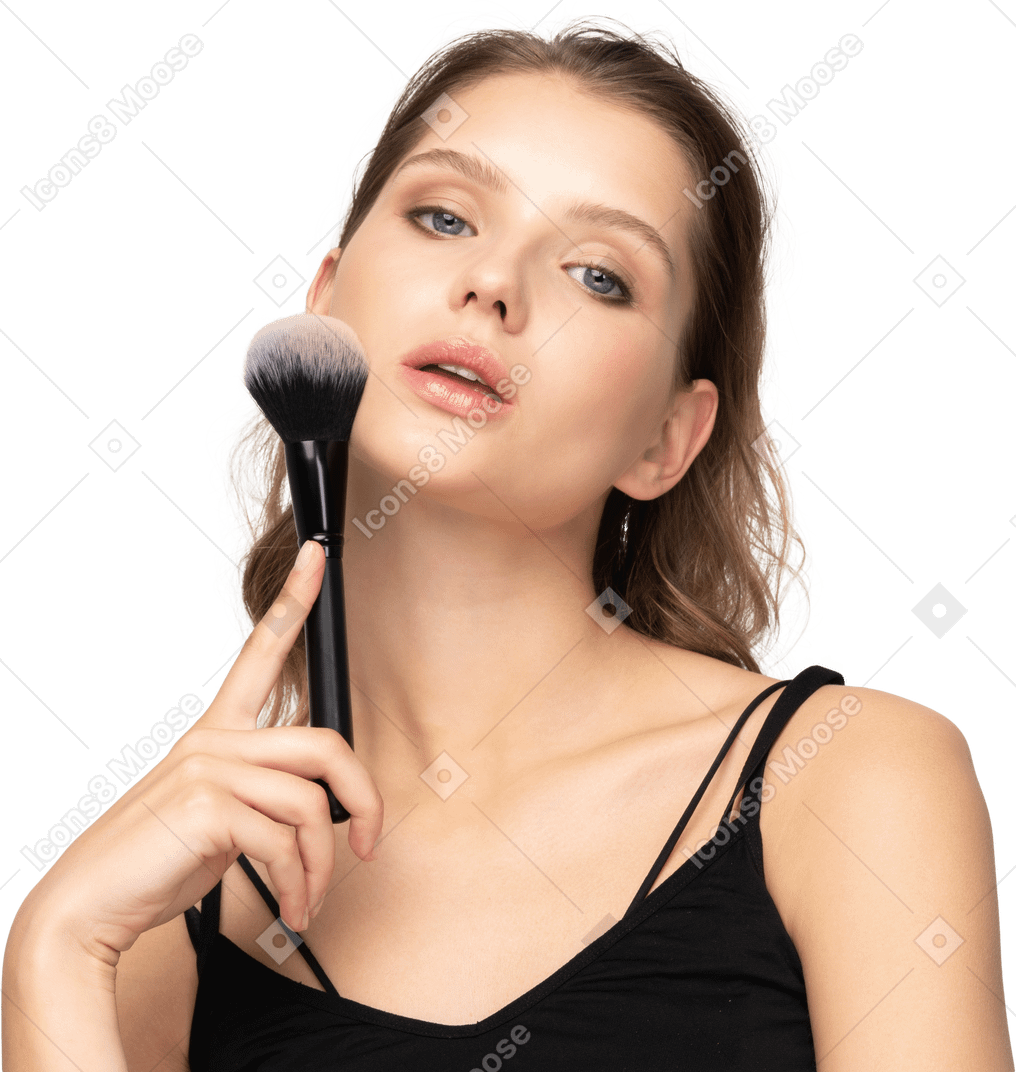 Vue de face d'une jeune femme sensuelle tenant un pinceau de maquillage