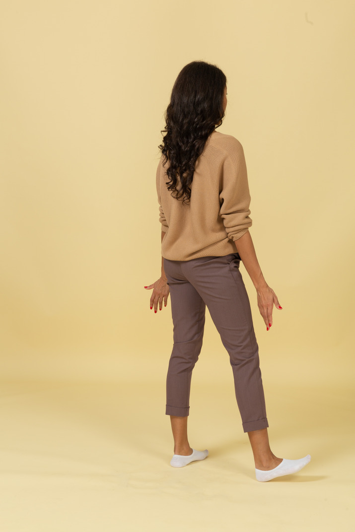 Three-quarter back view of a questioning dark-skinned young female outspreading her hands