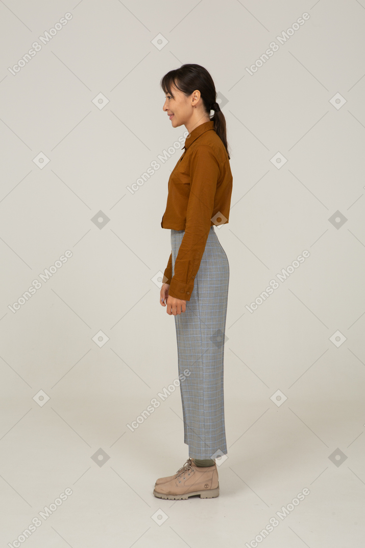Vue latérale d'une jeune femme asiatique souriante en culotte et chemisier debout immobile