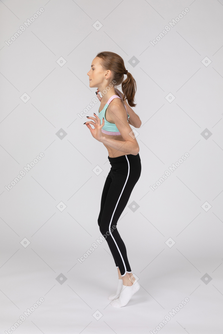 一个十几岁的女孩，一边站着脚尖举手的运动服的侧视图
