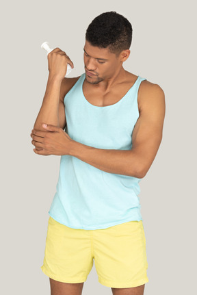 A man in a blue tank top applying sunscreen