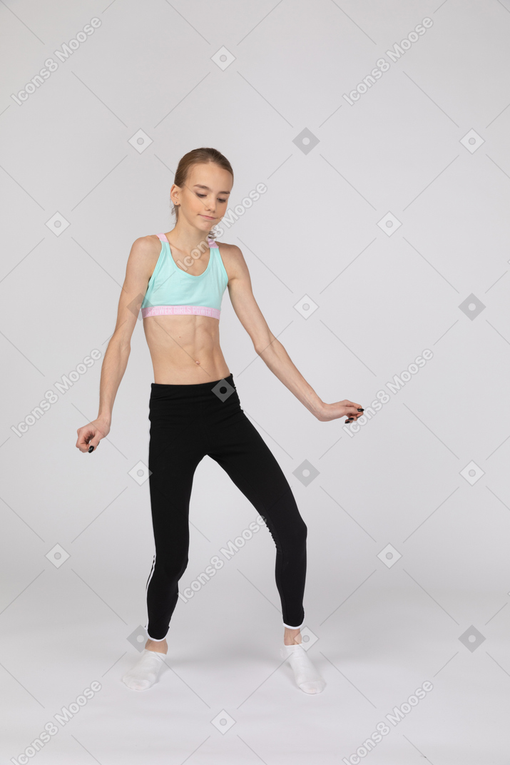 Three-quarter view of a teen girl in sportswear outspreading hands and bending knee