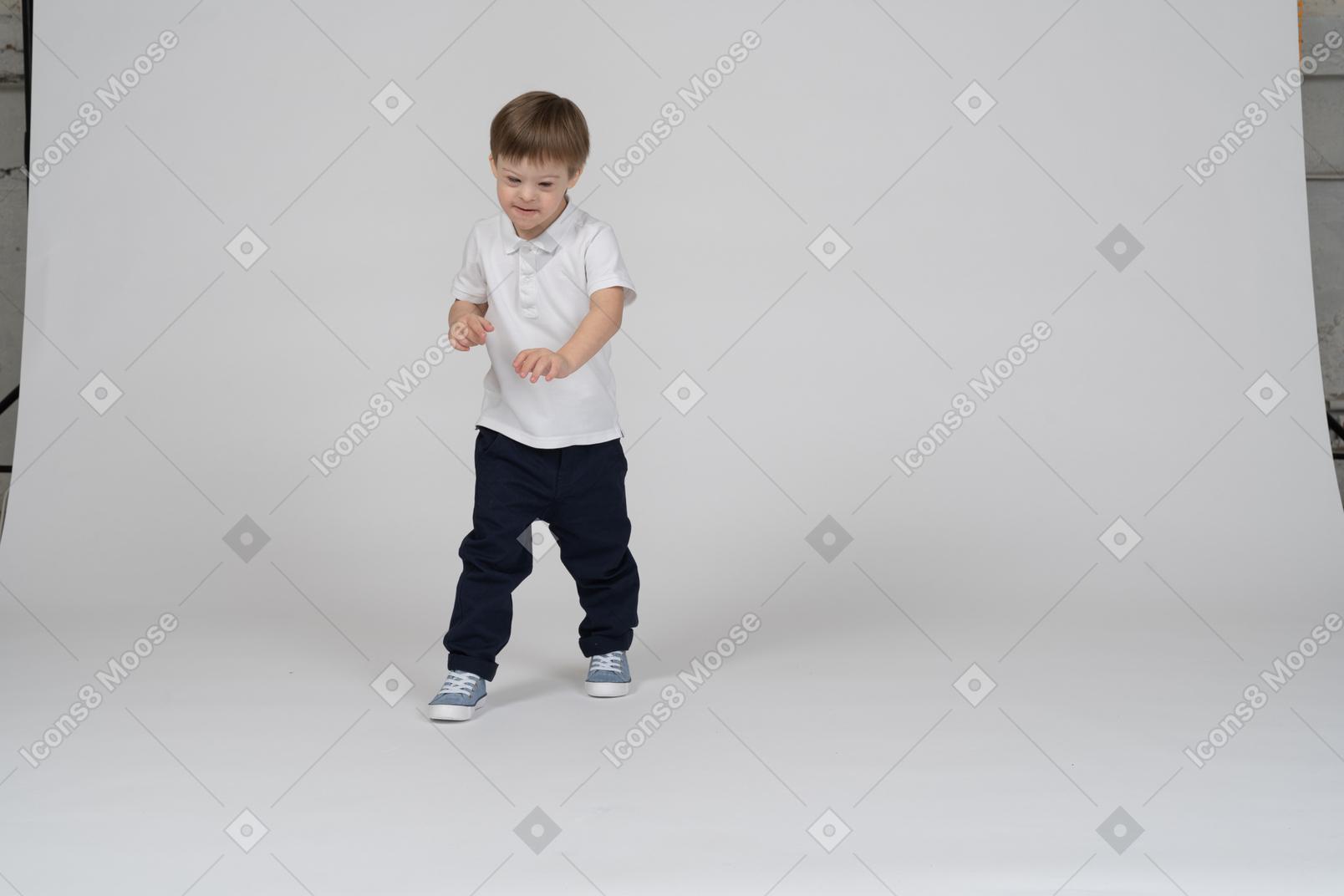 Vista frontal de un niño dando un paso adelante y mirando hacia abajo sonriendo
