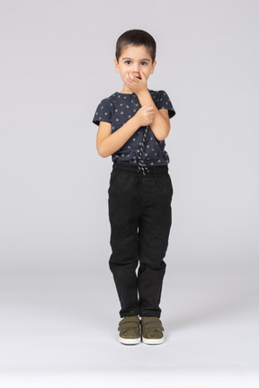 Вид спереди симпатичного мальчика, прикрывающего рот рукой и смотрящего в камеру