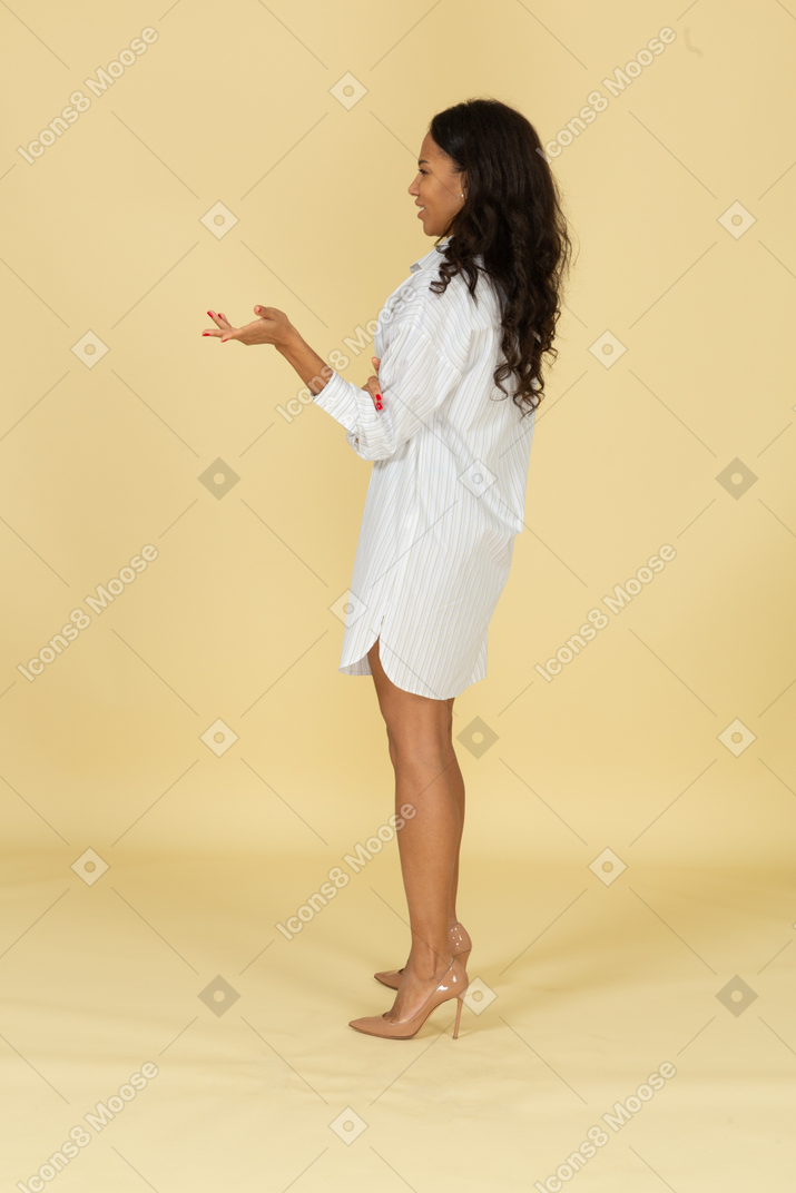 Vista laterale di una giovane femmina dalla carnagione scura interrogante in abito bianco